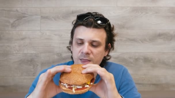 Joven comiendo una hamburguesa sentado en un café . — Vídeos de Stock