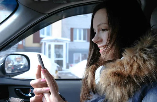 Uma mulher num carro com um telemóvel. Jovem bela mulher morena olhando algo no telefone celular . — Fotografia de Stock
