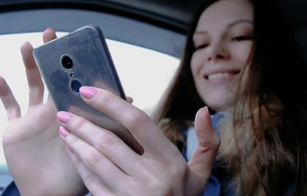Mujer en un coche con teléfono móvil. Joven hermosa mujer morena buscando algo en el teléfono móvil y y se ríe . — Foto de Stock