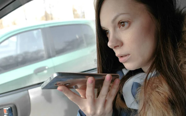 Jovem mulher bonita falar uma mensagem de voz em um telefone móvel sentado no carro . — Fotografia de Stock