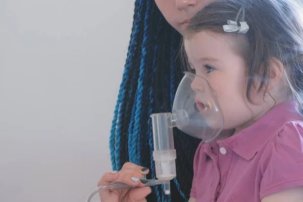 Девушка вдыхает через маску ингалятора со своей мамой. Использование ингалятора и распылителя для лечения . — стоковое фото