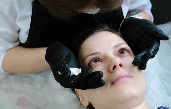 El cosmetólogo mira los ojos de los clientes. Botox y laminación de pestañas. Tratamiento de belleza . — Foto de Stock