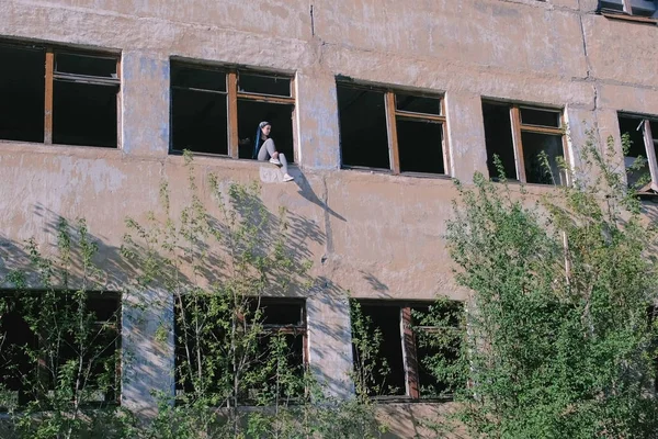 Женщина сидит на окне разрушенного многоэтажного здания со многими разбитыми окнами . — стоковое фото
