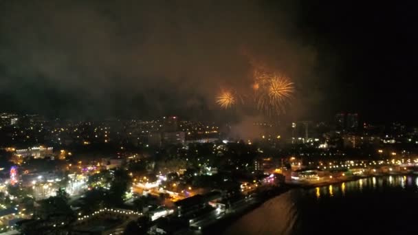 Slavnostní ohňostroj v malém městečku na pobřeží v noci. Letecký pohled na město, moře a ohňostroj. — Stock video