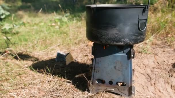 El hombre pone una olla en una estufa de horno de campamento de metal en maderas al aire libre . — Vídeo de stock