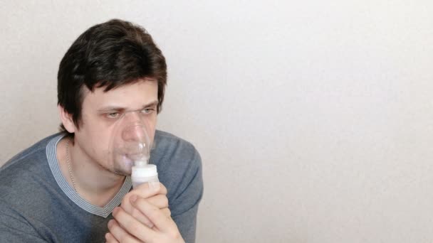 Используйте для лечения ингалятор и распылитель. Молодой человек вдыхает через маску ингалятора. Вид сбоку . — стоковое видео