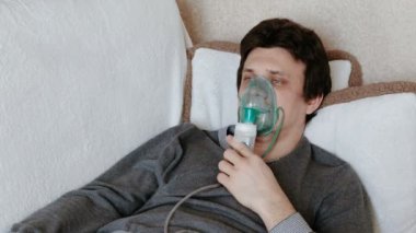 Nebulizatör ve astım tedavisi için kullanın. Genç adam kanepede yatan inhaler maskesi aracılığıyla teneffüs edilmesi. Önden Görünüm
