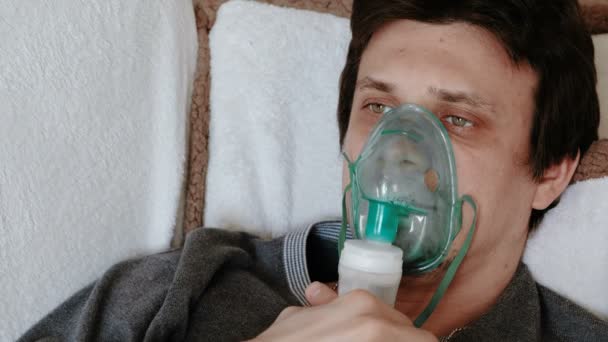 Use nebulizer and inhaler for the treatment. Closeup mans face inhaling through inhaler mask lying on the couch. Front view — Stock Video
