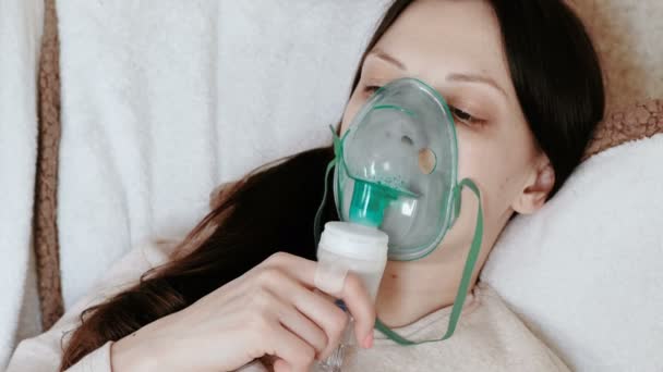 Use nebulizador e inhalador para el tratamiento. Mujer joven inhalando a través de la máscara del inhalador acostada en el sofá. Vista lateral . — Vídeo de stock