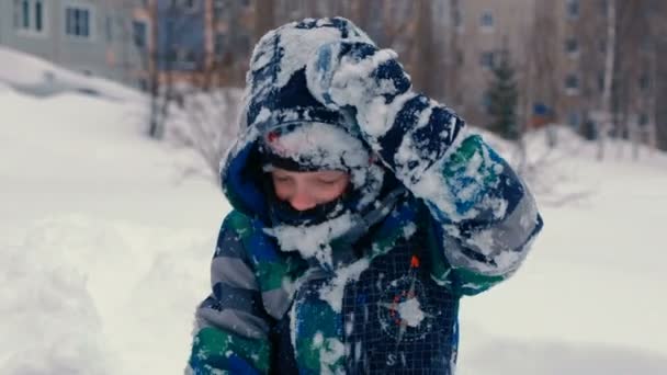 Menino joga na neve, olha para a câmera e sorrindo . — Vídeo de Stock