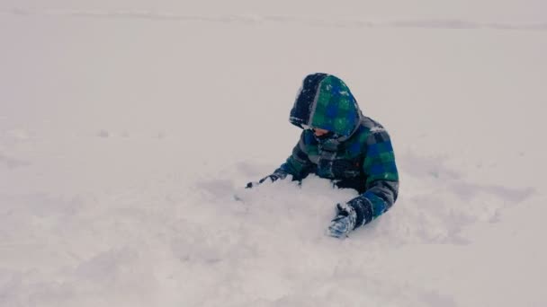 Le garçon s'enterre dans la neige, jouant avec la neige . — Video