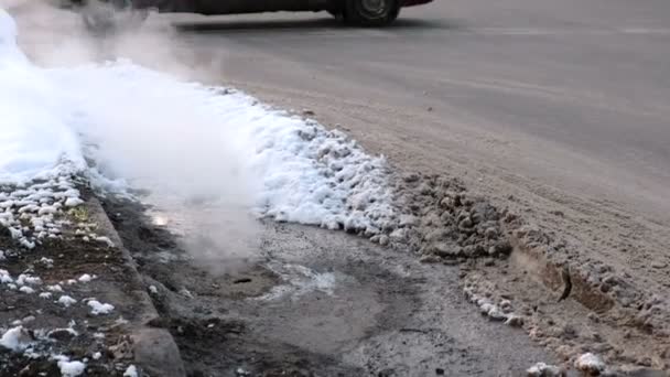 Steam jest od pokrywy kanalizacji sanitarnej w śniegu na poboczu drogi. Widok z przodu. — Wideo stockowe