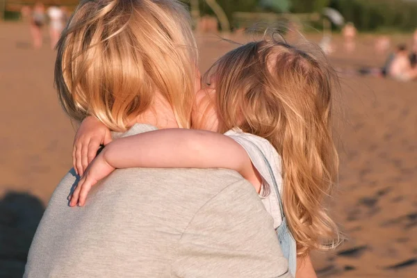 Linda loira mãe e filha abraçando na praia ao pôr do sol . — Fotografia de Stock