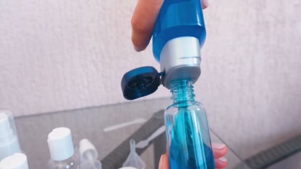 Las manos de las mujeres vierten gel de ducha azul en una pequeña botella de gran tamaño. Conjunto de frascos de viaje . — Vídeos de Stock