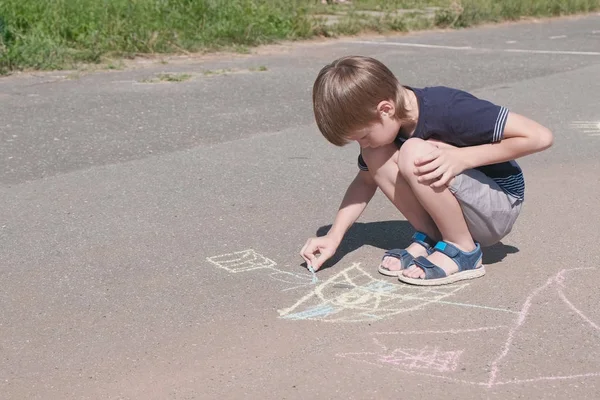 Chico dibuja un barco con tiza azul en el asfalto. Primer plano de las manos . —  Fotos de Stock