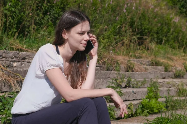 Молодая женщина говорит мобильный телефон сидя в парке . — стоковое фото