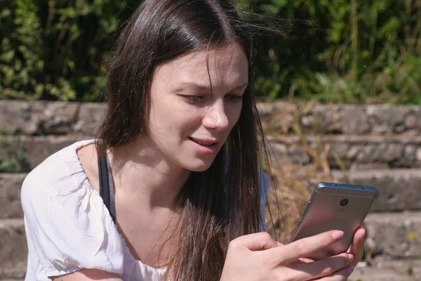 Женщина печатает сообщение по телефону сидя в парке и улыбаясь . — стоковое фото