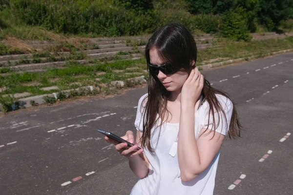 Chica morena joven caminando en el estadio en una zona residencial y mensajería en un teléfono móvil . — Foto de Stock