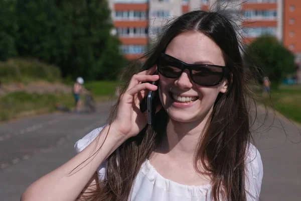 Menina morena jovem andando no estádio em uma área residencial e falando em um telefone celular . — Fotografia de Stock