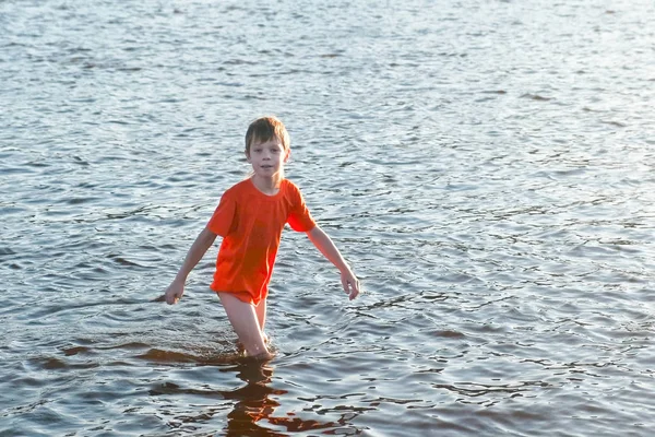 Niño en una camiseta roja camina sobre el agua del río . —  Fotos de Stock