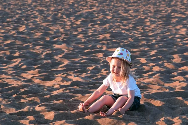 Chica jugando en la arena sentada en la playa . — Foto de Stock