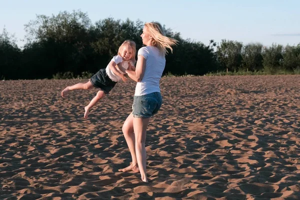 Matka i córka na plaży. Przędzenia matka z córką na rękach. — Zdjęcie stockowe