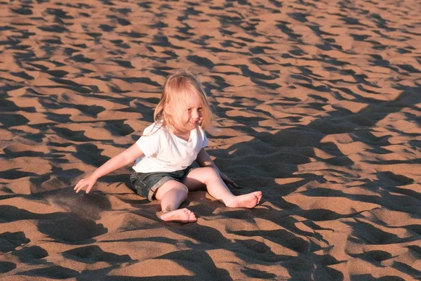 Flicka som leker i sanden sitter på stranden. — Stockfoto