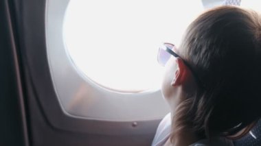 Tanınmayan çocuk güneş gözlüğü uçak pencereden dışarı görünüyor.