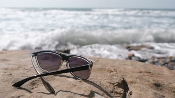 Denizin kenarında taş üzerinde güneş gözlüğü. — Stok video
