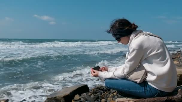 Woman photographs the sea waves sitting on the stones shore. — Stock Video
