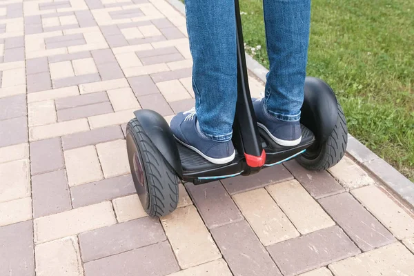 Personas piernas en zapatillas de deporte rodando en scooter giratorio en la carretera de pavimentación. Vista trasera . — Foto de Stock