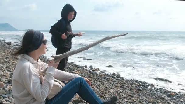 Mom and son play together on the beach. Shoot from branches as from the weapon. — Stock Video