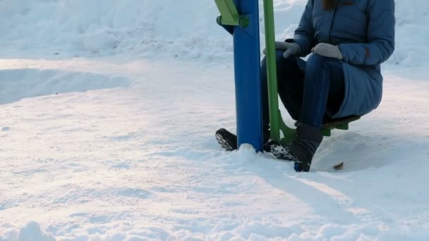 Pernas de mulher close-up está fazendo exercícios em simulador em um parque de inverno na cidade. Vista frontal . — Vídeo de Stock