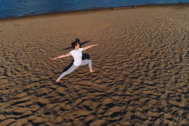 Şehrin nehrin yanında kum plaj üzerinde yoga yaparken kadın. Harika bir manzara.