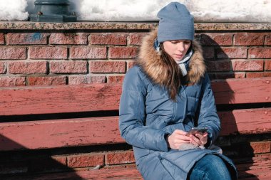 Kadın kış parkta oturan cep telefonunda internet sayfalarının gözatma.