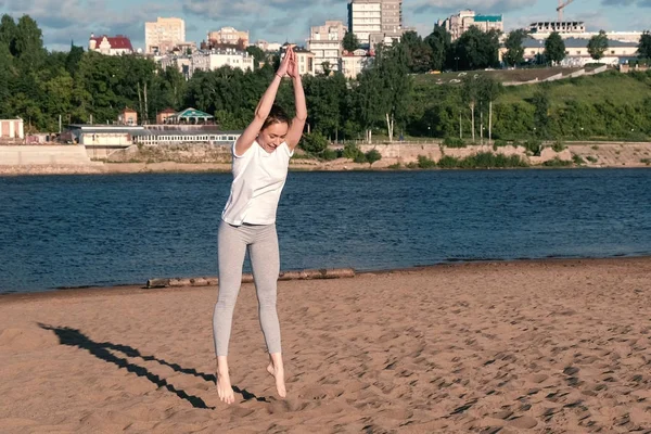 Kvinnan gör övningar sport på stranden av floden i staden. Hoppning. — Stockfoto