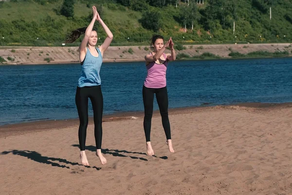 Två kvinna gör övningar sport på stranden av floden i staden. Hoppning. — Stockfoto