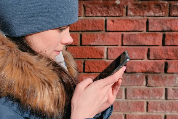 Mulher está navegando páginas da internet no telefone móvel sentado no parque de inverno. Vista lateral do rosto close-up . — Fotografia de Stock