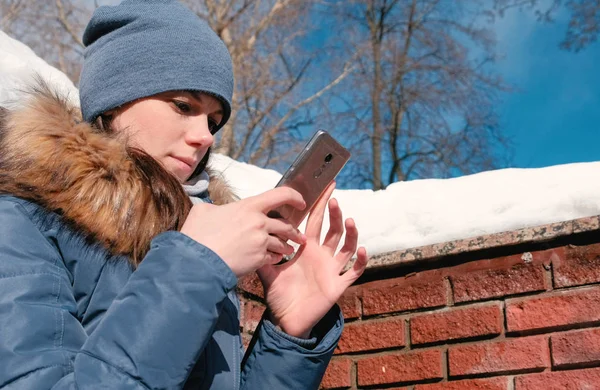 Mujer está escribiendo un mensaje en el teléfono móvil sentado en el parque de invierno . — Foto de Stock