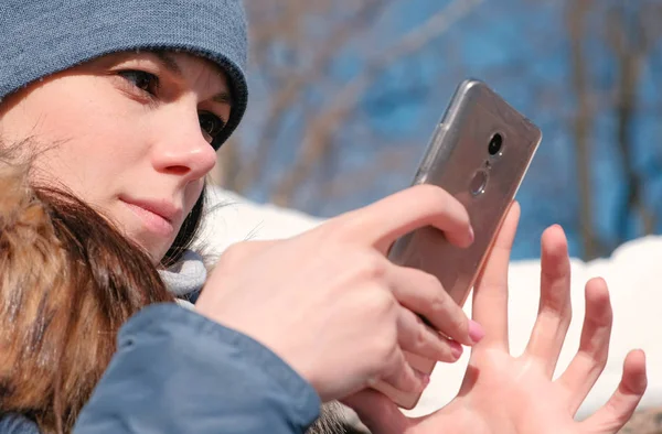 Mujer está navegando páginas de Internet en el teléfono móvil sentado en el parque de invierno. Cara de primer plano . — Foto de Stock