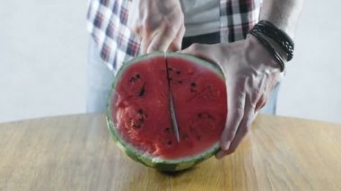 Adam karpuz yarısı mutfak masasında iki parçaya böler. Eller yakın çekim.