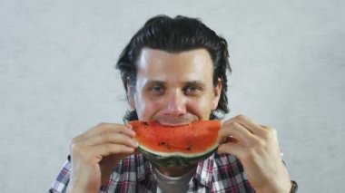 Brunet adam beyaz arka plan üzerinde sulu karpuz yiyor.