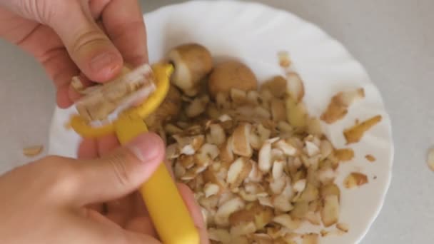 Mans hands is peeling potato with yellow peeler on the plate. — Stock Video