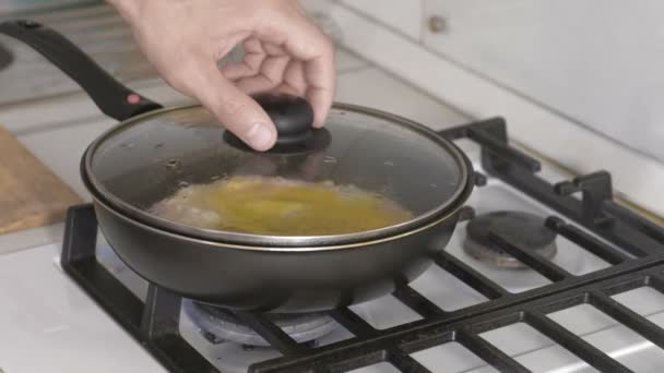 Mans mão abre a tampa de preparar ovos mexidos com salsicha em uma frigideira no fogão a gás . — Vídeo de Stock