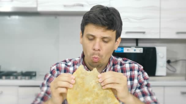 Jonge man in een plaid shirt eet een grote cheburek met een eetlust. — Stockvideo