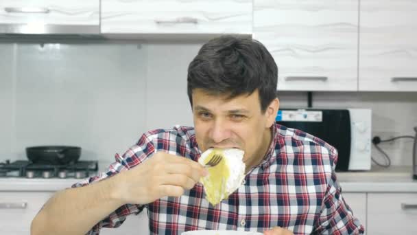 Jovem de camisa xadrez comendo ovos mexidos sentados à mesa . — Vídeo de Stock