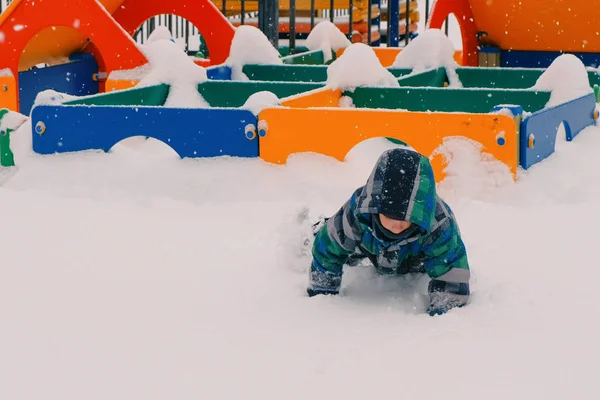 Ragazzo strisciare attraverso i cumuli di neve sul parco giochi . — Foto Stock