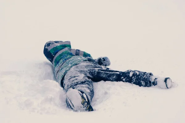 Menino deitado na neve rolando de um lado para o outro . — Fotografia de Stock
