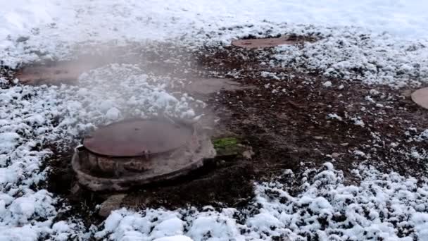 Close-up steam is from sanitary sewer cover in snow in winter park. Melted snow around. — Stock Video