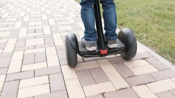 Onherkenbaar jongen ontwikkelt op gyro scooter in de buurt van het huis. Achteraanzicht. Close-up van de benen. — Stockvideo